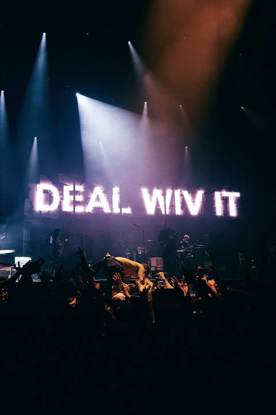 Concertgoers reach toward a band on stage under neon lights.