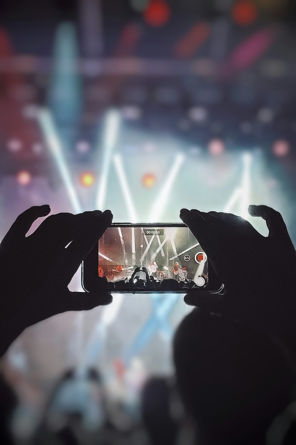 Hands hold a smartphone recording a concert stage.