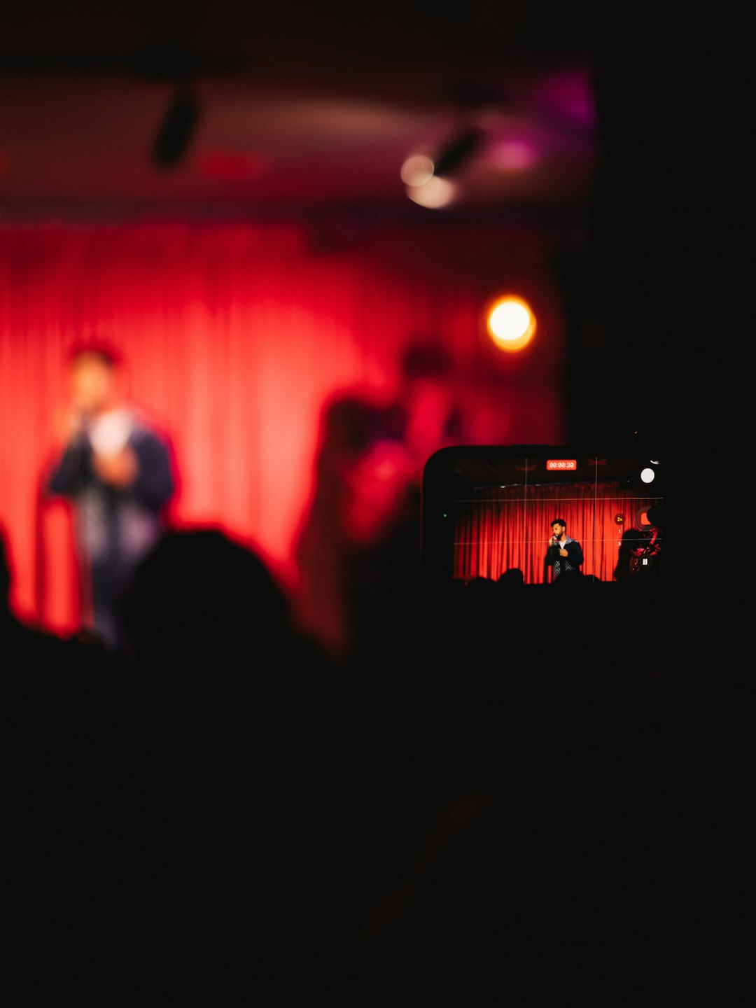 A concertgoer records a singer performing on a stage.